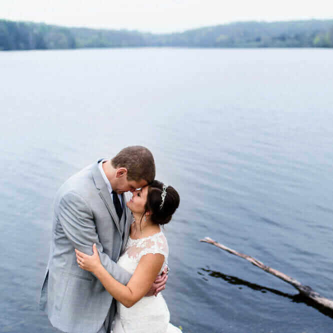 A bride and groom kiss in front of a lake.